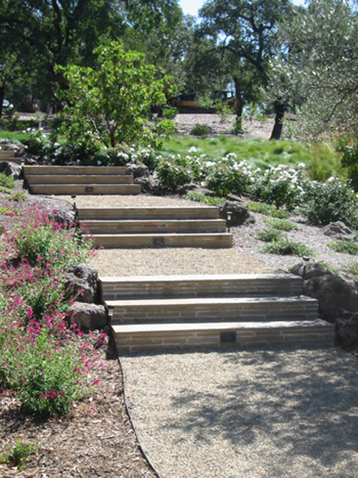 This wine country garden uses stone steps and pathways to link outdoor activities. Water resistant plants and outdoor lighting offer a beautiful way to get from the pool area to the deck and garden areas below.